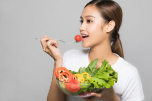 A beautiful Asian woman that is eating from a bowl of fresh veggies.