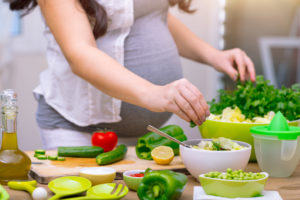Pregnant woman that is preparing food with healthy fruits and veggies.