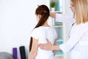 A health professional checking a young girl's back for scoliosis.