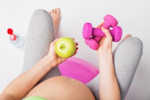 Pregnant woman with an apple and weights in her hands